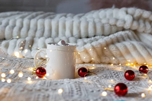 Noel ya da yeni yıl sıcak çikolatası, şekerleme, hafif çelenk ve beyaz bir yatakta kırmızı Noel ağacı oyuncakları, seçici bir odak.