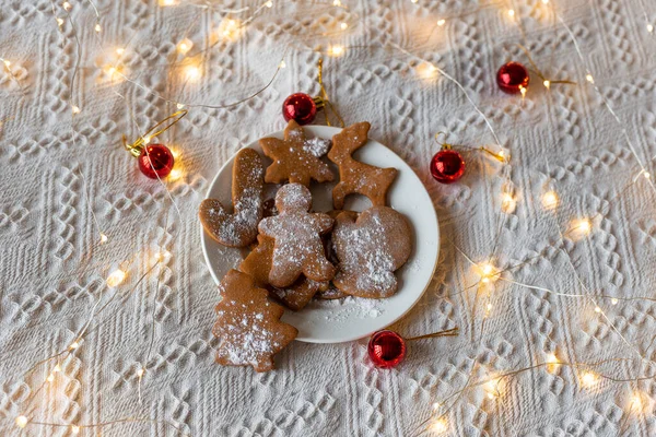 Noel ya da yeni yıl kurabiyesi beyaz battaniyeli ve hafif çelenkli bir yatakta. Kırmızı Noel oyuncakları. Seçici odak