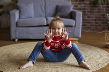 Kırmızı Noel süveterli küçük tatlı kız oturma odasında oynuyor.