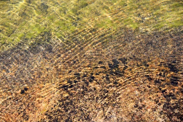 Küçük dalgaların gölgesiyle gölün dibindeki bir taşın resmi.