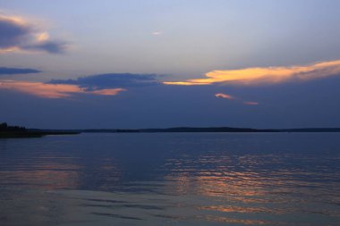 Sessiz göl suyunun üzerindeki mavi bulutların ardında gün batımı