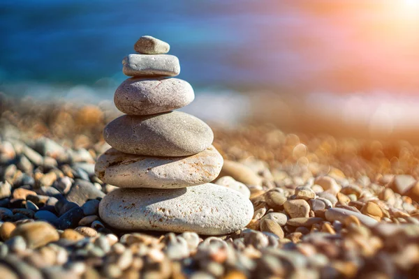 Balanced Pebbles Pyramid on the Beach on Sunny Day and Clear Sky at Sunset. Blue Sea on Background Selective focus, zen stones on sea beach, meditation, spa, harmony, calm, balance concept