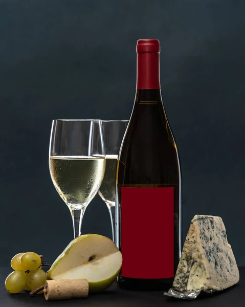 composition with glass and bottle of white wine with blue mold cheese, pear and grapes on grey background. copy space