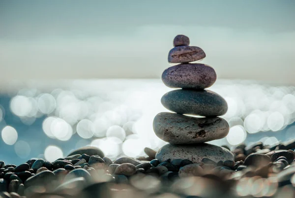 Balanced Pebbles Pyramid on the Beach on Sunny Day and Clear Sky at Sunset. Blue Sea on Background. Selective focus, Bokeh. Zen stones on sea beach, meditation, spa, harmony, calm, balance concept.