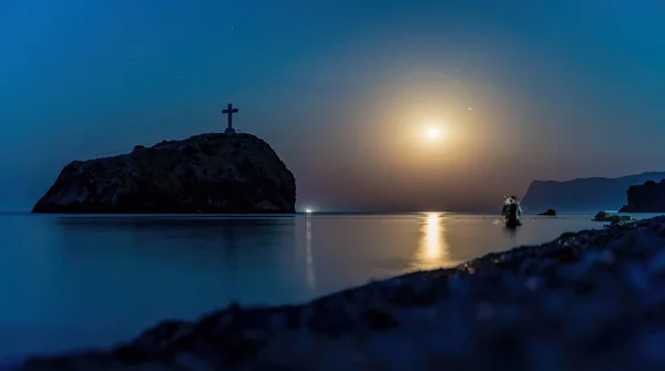 Starry night with a full moon over sea, cape Fiolent. Jasper beach and rock of the holy phenomenon with a cross on the background of the moon