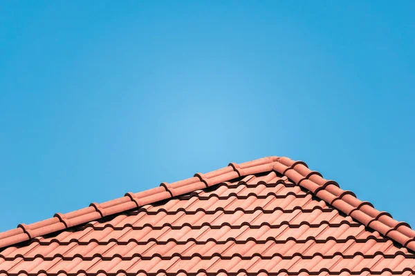 Brown tile roof under blue sky. The photo is divided on two part. One part is a roof made of clay tiles and the other is a blue sky. Brown surface of tile roof with natural color, texture and pattern.