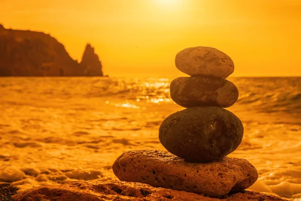 Balanced Pebbles Pyramid on the Beach on Sunny Day and Clear Sky at Sunset. Blue Sea on Background Selective focus, zen stones on sea beach, meditation, spa, harmony, calm, balance concept.