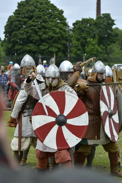 Armed knights in chain mail, helmets and red-white shields perform a combat structure at the historic festival of reenactors — Stock Photo, Image