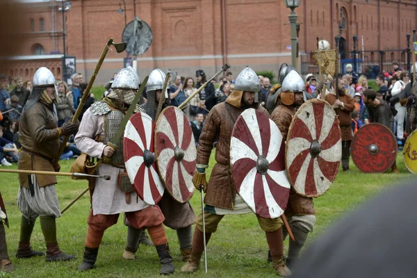 Armed knights in chain mail, helmets and white- red shields perform a combat structure at the historic festival of reenactors — Stock Photo, Image