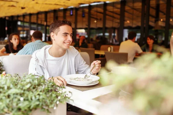 Güzel, neşeli adam restoranın yaz terasında yemek ve içeceklerle rahatlıyor. Yazın güneşli bir günde, terasta dinlenmek