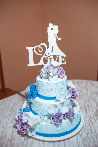 A beautiful blue wedding cake decorated with creamy white and purple flowers with the silhouette of a bride and groom. I love you inscription.