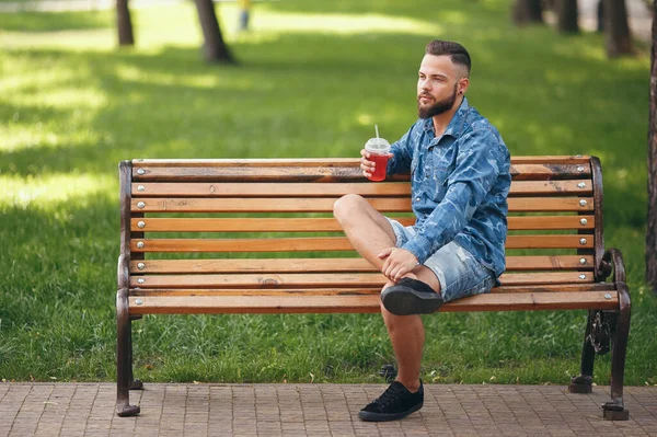 Un tipo con limonada está descansando en un parque en un banco en primavera. Día soleado . — Foto de Stock
