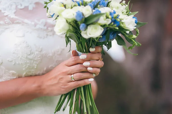 Una novia en un hermoso vestido con un tren sosteniendo un ramo de flores y vegetación —  Fotos de Stock