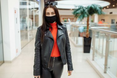 Siyah maskeli bir kız alışveriş merkezi boyunca yürüyor. Koronavirüs salgını. Koruyucu maskeli bir kız alışveriş merkezinde alışveriş yapıyor.