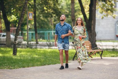 Güzel, aşık genç bir çift soğuk limonatayla yaz parkında yürüyor. Romantik çift temiz havada buluşuyor.