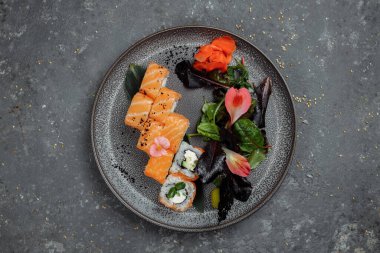 Somon balıklı lezzetli suşi ruloları ve gri tabakta gri taştan arka planda Philadelphia peyniri. Geleneksel Japon deniz ürünleri, sağlıklı gıda konsepti.