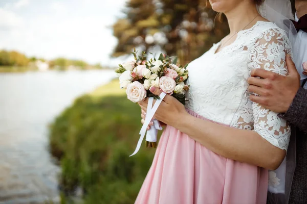 Una novia en un hermoso vestido con un tren sosteniendo un ramo de flores y vegetación —  Fotos de Stock