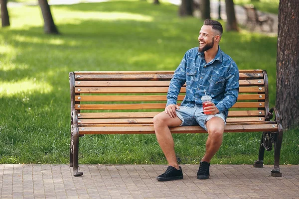 Un tipo con limonada está descansando en un parque en un banco en primavera. Día soleado . — Foto de Stock