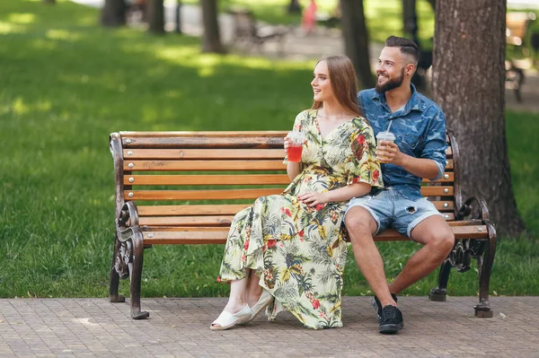 Moda jovem casal adolescente descansando em um parque da cidade com bebidas sentadas em um banco em um dia ensolarado de verão — Fotografia de Stock