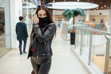 Siyah maskeli bir kız alışveriş merkezi boyunca yürüyor. Koronavirüs salgını. Maskeli bir kadın alışveriş merkezinde duruyor. Koruyucu maskeli bir kız alışveriş merkezinde alışveriş yapıyor..