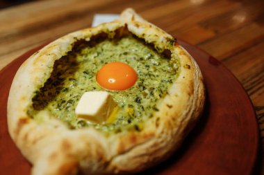 Khachapuri, ıspanaklı, erimiş peynirli ve tereyağlı lezzetli hamur hamurundan yapılmıştır. Geleneksel Hachapuri Spinacia ile Tepelendi Tahta Kırsal Arkaplanda Yapraklar
