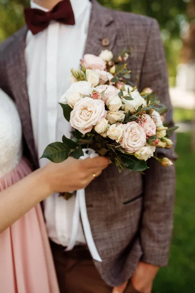 Una novia en un hermoso vestido con un tren sosteniendo un ramo de flores y vegetación —  Fotos de Stock