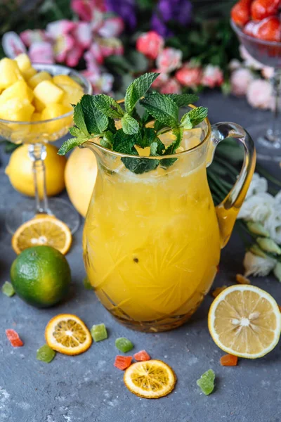 Nyári hideg italok. Jeges limonádé a kancsóban citrommal és narancs mentával az asztalon a szabadban. Narancs limonádé egy kancsóban — Stock Fotó