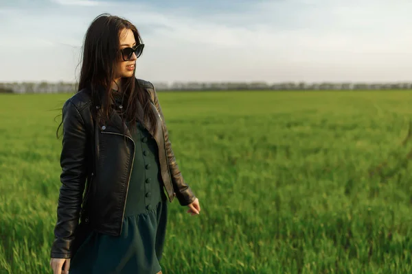 Retrato de comprimento total de uma menina elegante andando ao longo de um campo verde. Uma jovem mulher sorrindo está andando na natureza. Prado de primavera verde — Fotografia de Stock