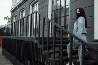 Balkonda koruyucu maskeli bir kız boş bir şehre bakıyor.