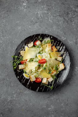 Gri arka planda siyah tabakta taze Sezar salatası. Üst görünüm.