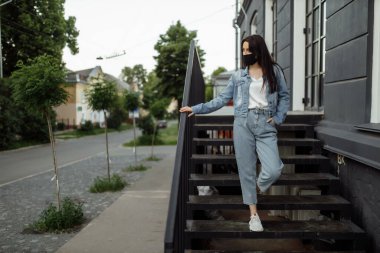 Balkonda koruyucu maskeli bir kız boş bir şehre bakıyor..