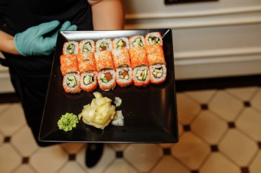 El Garsonu elinde taze suşi tabağı geleneksel restoranda Japon çiğ balığı tutuyor. Philadelphia taze Rolls Royce suşi barında servis ediliyor. Eldivenli garsonun elinde suşi var..