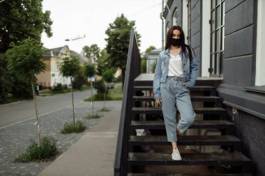 Balkonda koruyucu maskeli bir kız boş bir şehre bakıyor..