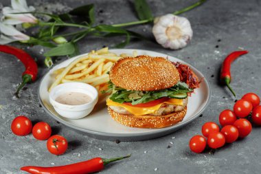 Peynirli hindi burger, marul, domates ve taze salatalık. Gri bir zemin üzerinde hindili pirzola ve patates kızartması sosu ve salata..