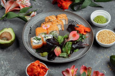 Somon balıklı lezzetli suşi ruloları ve gri tabakta gri taştan arka planda Philadelphia peyniri. Geleneksel Japon deniz ürünleri, sağlıklı gıda konsepti..