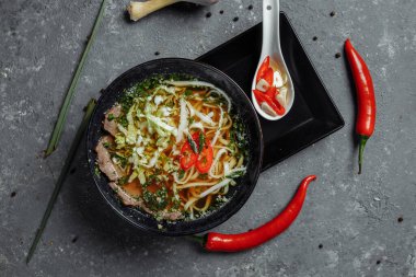 Asya mutfağı, arka planda siyah tabakta sığır eti çorbası. Baharatlı biftek çorbası, sığır filetosu, udon eriştesi, kırmızı biber ezmesi, Pekin lahanası, acı biber, kişniş, seçilmiş sos.