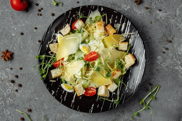 Gri arka planda siyah tabakta taze Sezar salatası. Üst görünüm.