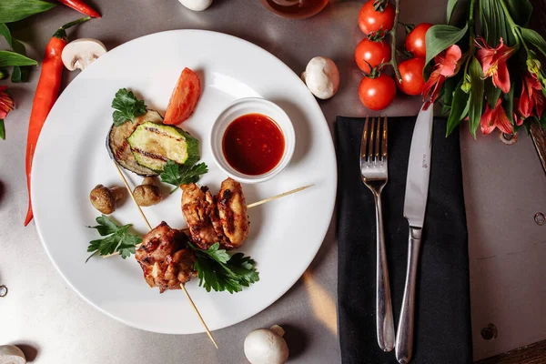 Barbecued marinated turkey or chicken meat shish kebab skewers with ketchup sauce and grilled vegetables on rustic wooden table background. Traditional barbecue grill food.