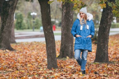 Güzel kız sonbahar parkında yürüyor. Sarı sonbahar parkında ceketli ve şapkalı bir kız..