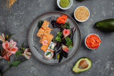 Somon balıklı lezzetli suşi ruloları ve gri tabakta gri taştan arka planda Philadelphia peyniri. Geleneksel Japon deniz ürünleri, sağlıklı gıda konsepti.