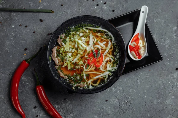 Asian cuisine, Beef soup fo in a black plate on a dark background. Soup Fo with Spicy beef broth, beef tenderloin, udon noodles, chili paste — Stock Image Asian cuisine, Beef soup fo in a black plate on a dark background. Soup Fo with Spicy beef broth, beef tenderloin, udon noodles, chili paste Stock Image