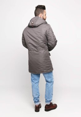 Beyaz kazaklı, mavi kotlu, gri ceketli, beyaz arka planda poz veren genç Avrupalı bir adam. Ceket reklamı için fotoğraf konsepti.