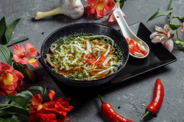 Asya mutfağı, arka planda siyah tabakta sığır eti çorbası. Baharatlı biftek çorbası, sığır filetosu, udon eriştesi, kırmızı biber ezmesi, Pekin lahanası, acı biber, kişniş, seçilmiş sos.