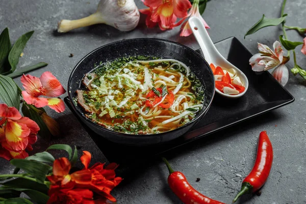 Asian cuisine, Beef soup fo in a black plate on a dark background. Soup Fo with Spicy beef broth, beef tenderloin, udon noodles, chili paste, Beijing cabbage, chili pepper, cilantro, Picked sauce — Stock Image Asian Cuisine Beef Soup Black Plate Dark Background Soup Spicy Stock Picture