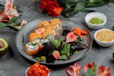 Somon balıklı lezzetli suşi ruloları ve gri tabakta gri taştan arka planda Philadelphia peyniri. Geleneksel Japon deniz ürünleri, sağlıklı gıda konsepti..