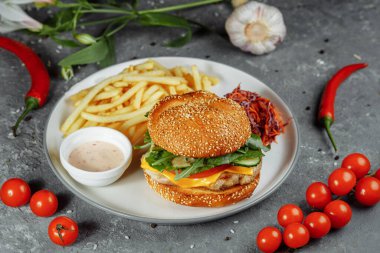 Peynirli hindi burger, marul, domates ve taze salatalık. Gri bir zemin üzerinde hindili pirzola ve patates kızartması sosu ve salata..