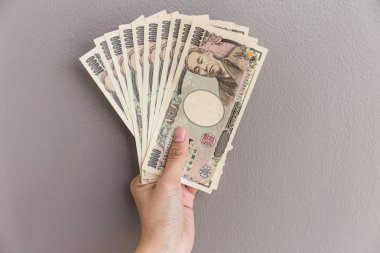 İşkadını vererek para ve holding 10.000 Japon yeni para el üzerinde duvar arka plan, Japon yeni mali ve iş kavramı gri