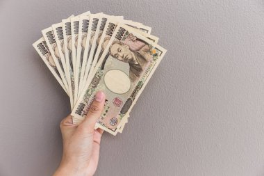 İşkadını vererek para ve holding 10.000 Japon yeni para el üzerinde duvar arka plan, Japon yeni mali ve iş kavramı gri