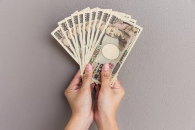 İşkadını vererek para ve holding 10.000 Japon yeni para el üzerinde duvar arka plan, Japon yeni mali ve iş kavramı gri