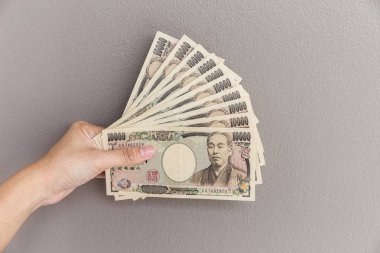 İşkadını vererek para ve holding 10.000 Japon yeni para el üzerinde duvar arka plan, Japon yeni mali ve iş kavramı gri